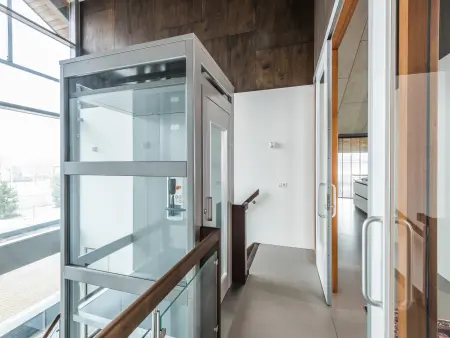 Hal met een glazen lift en een open deuropening naar een keuken. Modern interieurontwerp.