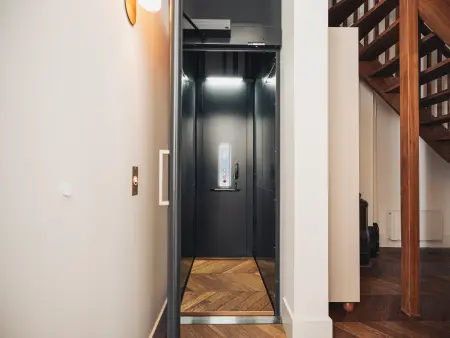 Lift met open deur in een modern interieur. Voorzien van houten vloeren, nabijgelegen trap en bedieningspanelen.
