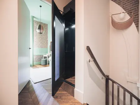 Modern interieur met een donkere deur naar de trap, een lichte deur naar een slaapkamer, houten vloeren en unieke verlichtingsarmaturen.